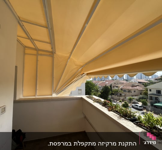סוכך צהוב נפרש מעל מרפסת עם צמחייה